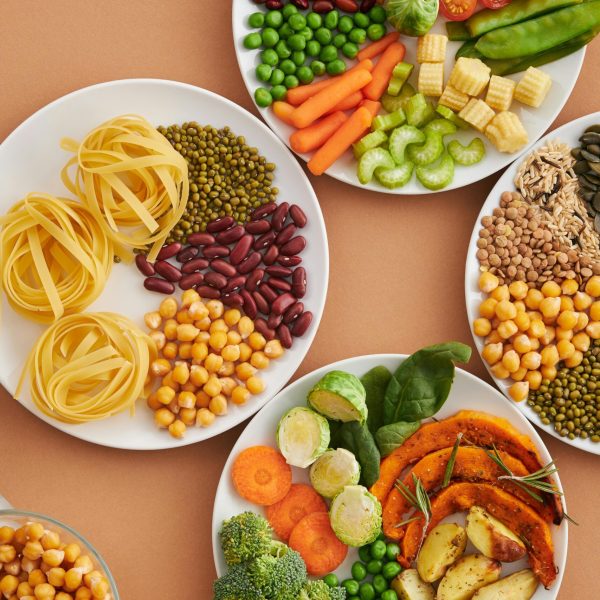 A vibrant mix of legumes, vegetables, nuts, and pasta arranged on white plates showcasing a balanced, healthy diet.